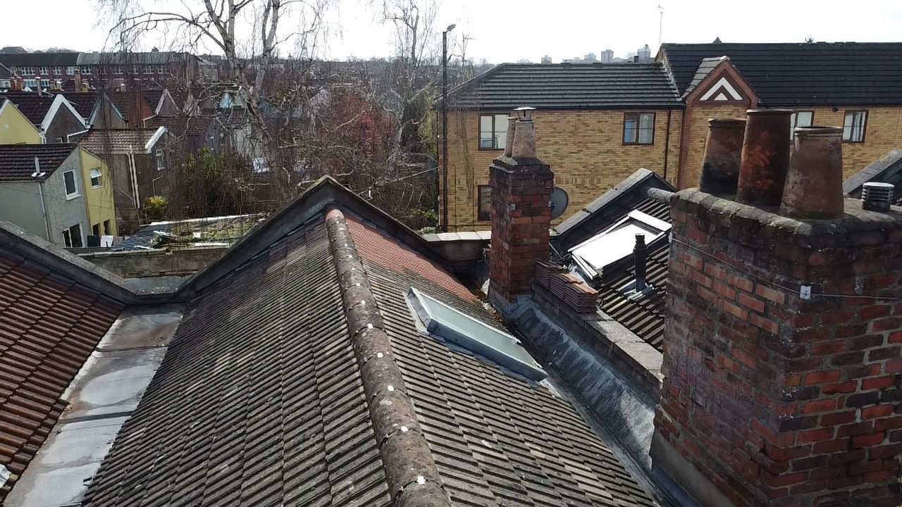 Rooftops of brick houses with chimneys and skylights in a residential neighborhood.