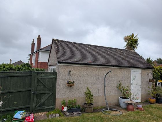 Backyard shed with gray roof, potted plants, and green gate under a cloudy sky