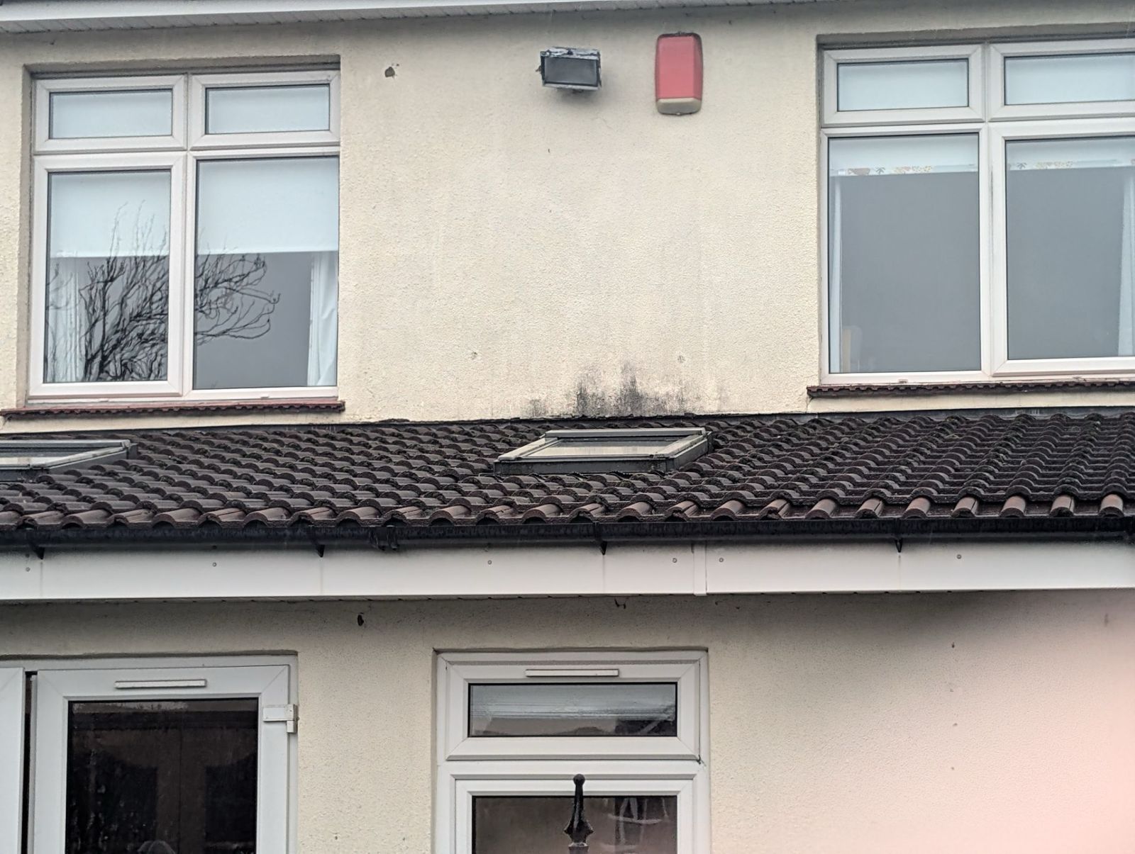 House exterior with white windows, dark tiled roof, and a red wall-mounted box above the roofline