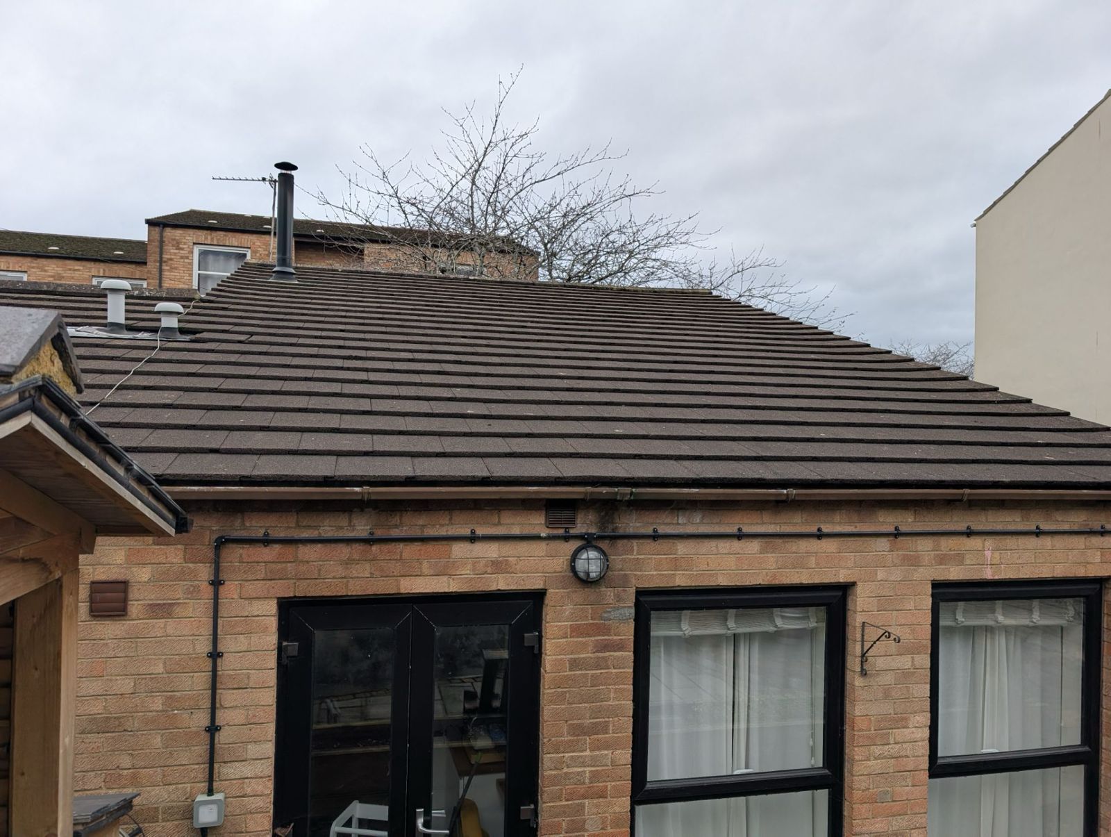 Brick house with a dark shingled roof, front door, and two windows under an overcast sky