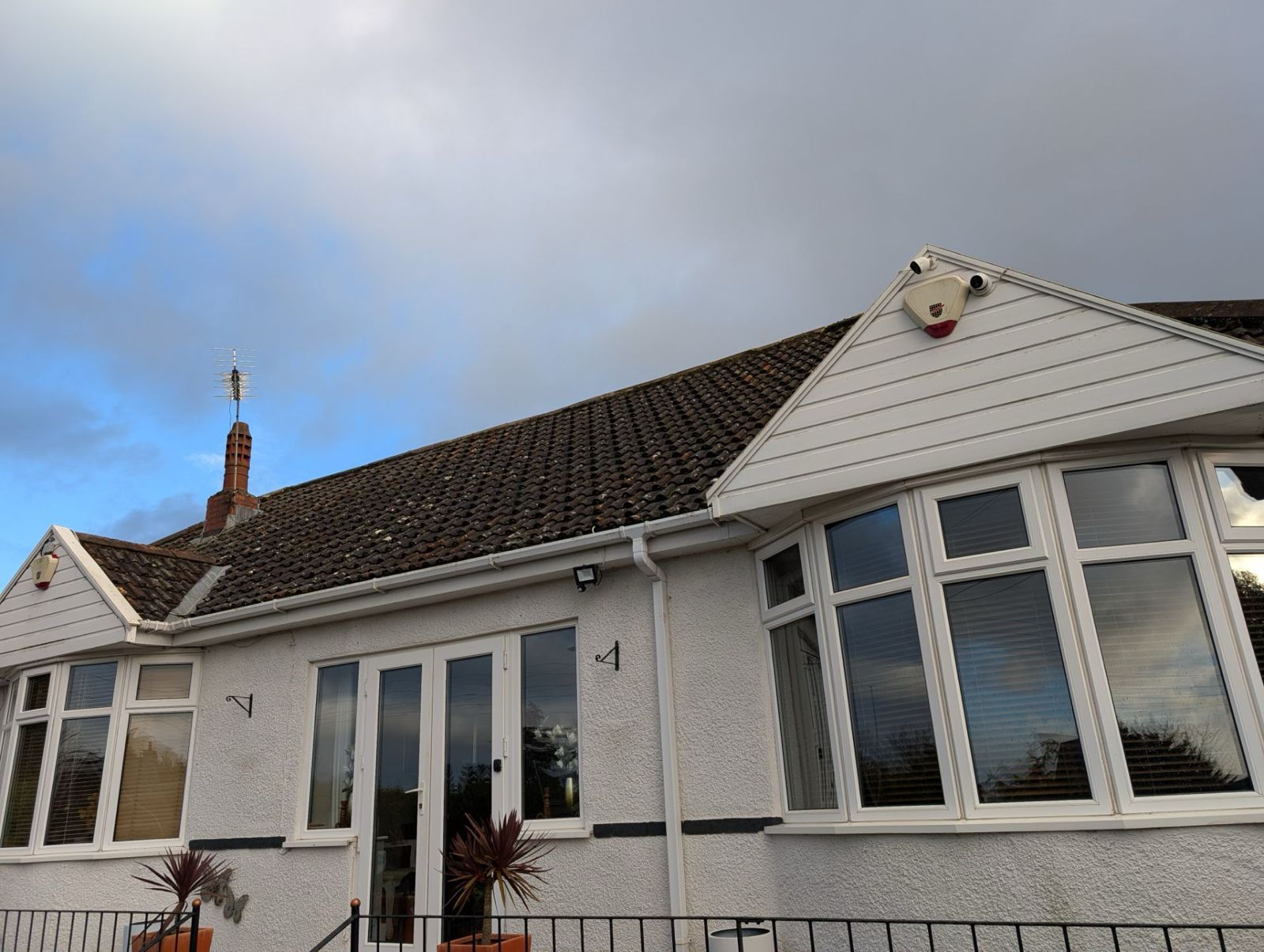 White bungalow exterior with dark tiled roof and large front windows under a cloudy sky