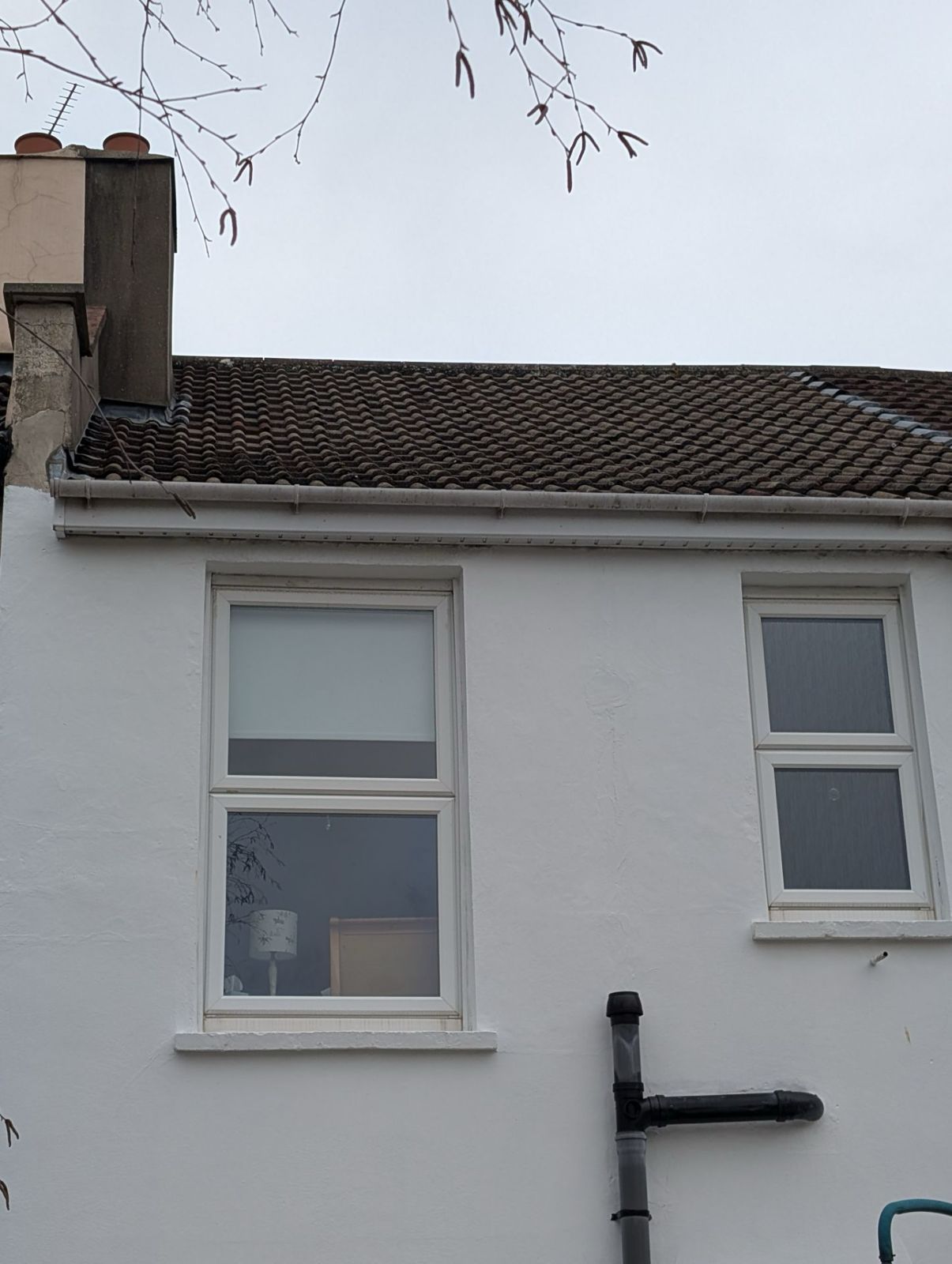 White house wall with two windows and a tiled roof under an overcast sky.