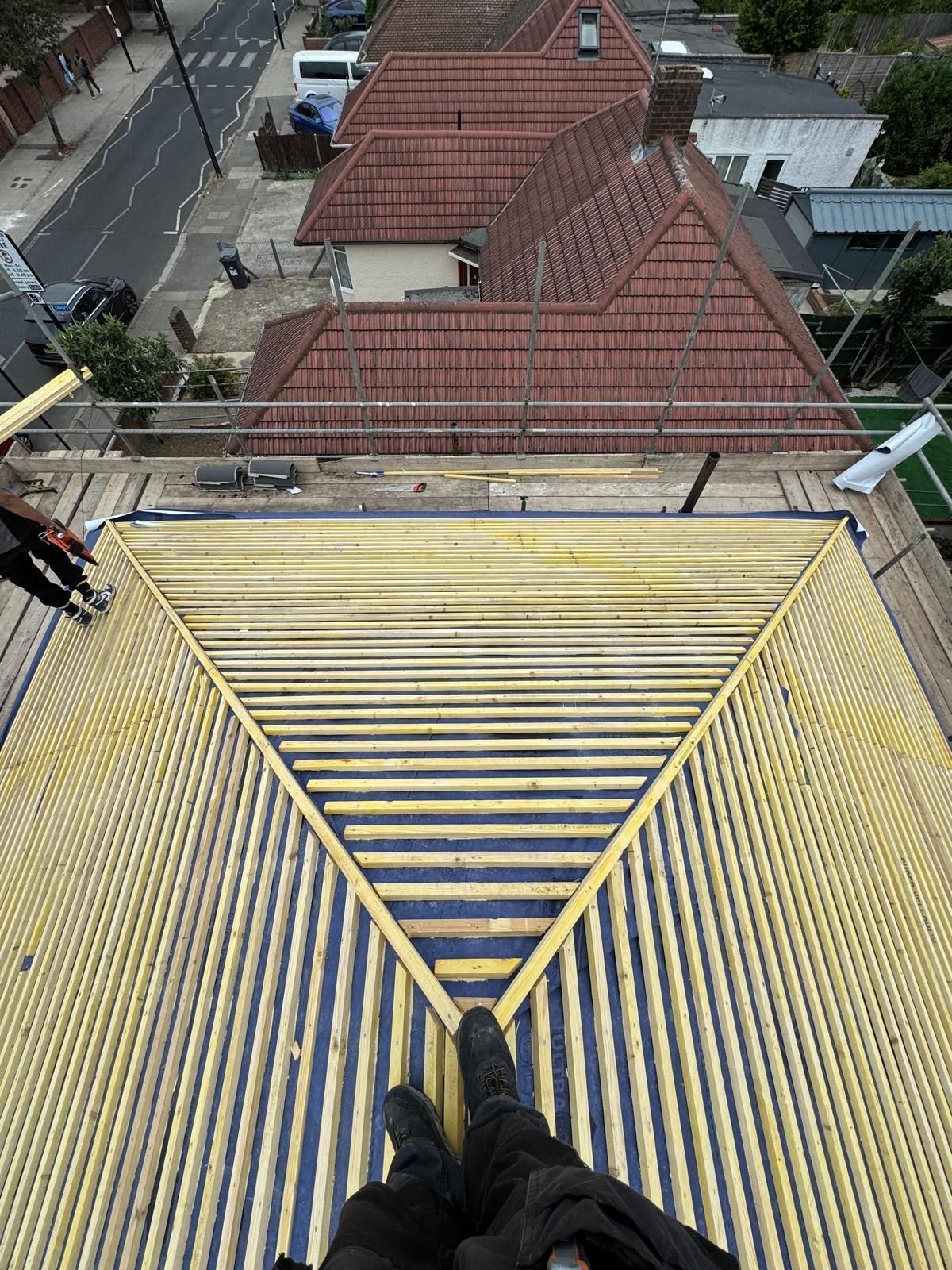 Looking down from a rooftop onto red-tiled houses and street below, with feet on a yellow metal roof edge