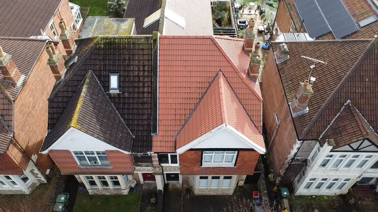 Aerial view of two brick houses with red roofs, solar panels, and a fenced back garden.