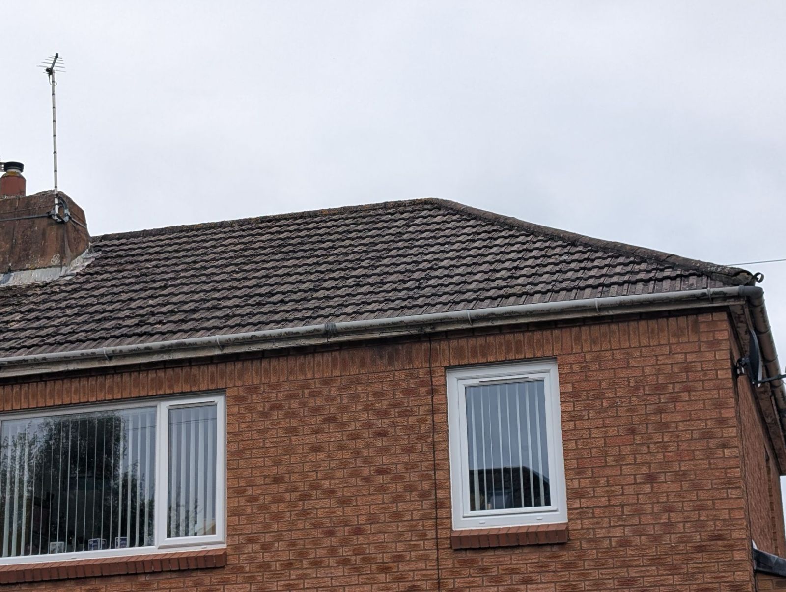 Brick house with a dark tiled roof and white-framed windows under a cloudy sky