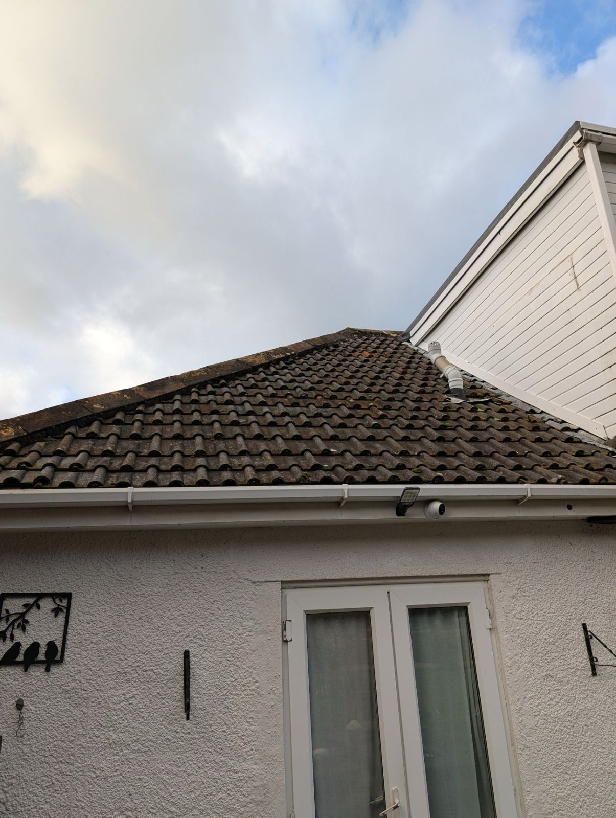 House roof and upper facade with white walls, dark tiled roof, and cloudy sky above