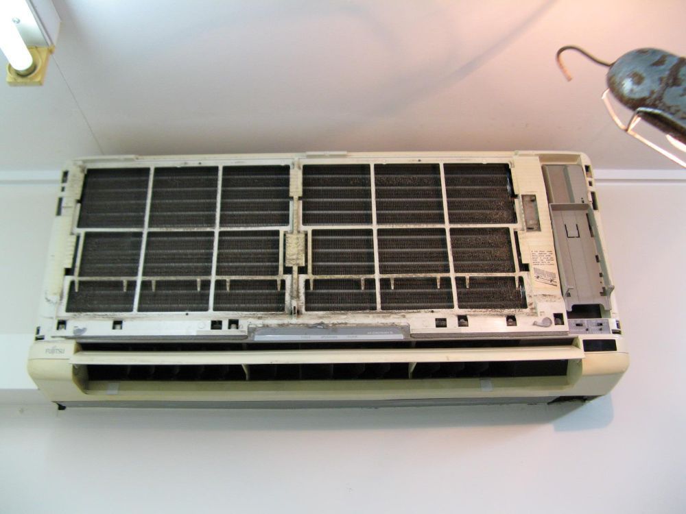 A Dirty Air Conditioner is Hanging on a White Wall — Air-Con Cleaning Specialists in Mossman, QLD