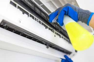 A Person is Cleaning an Air Conditioner With a Spray Bottle — Air-Con Cleaning Specialists in Redlynch, QLD