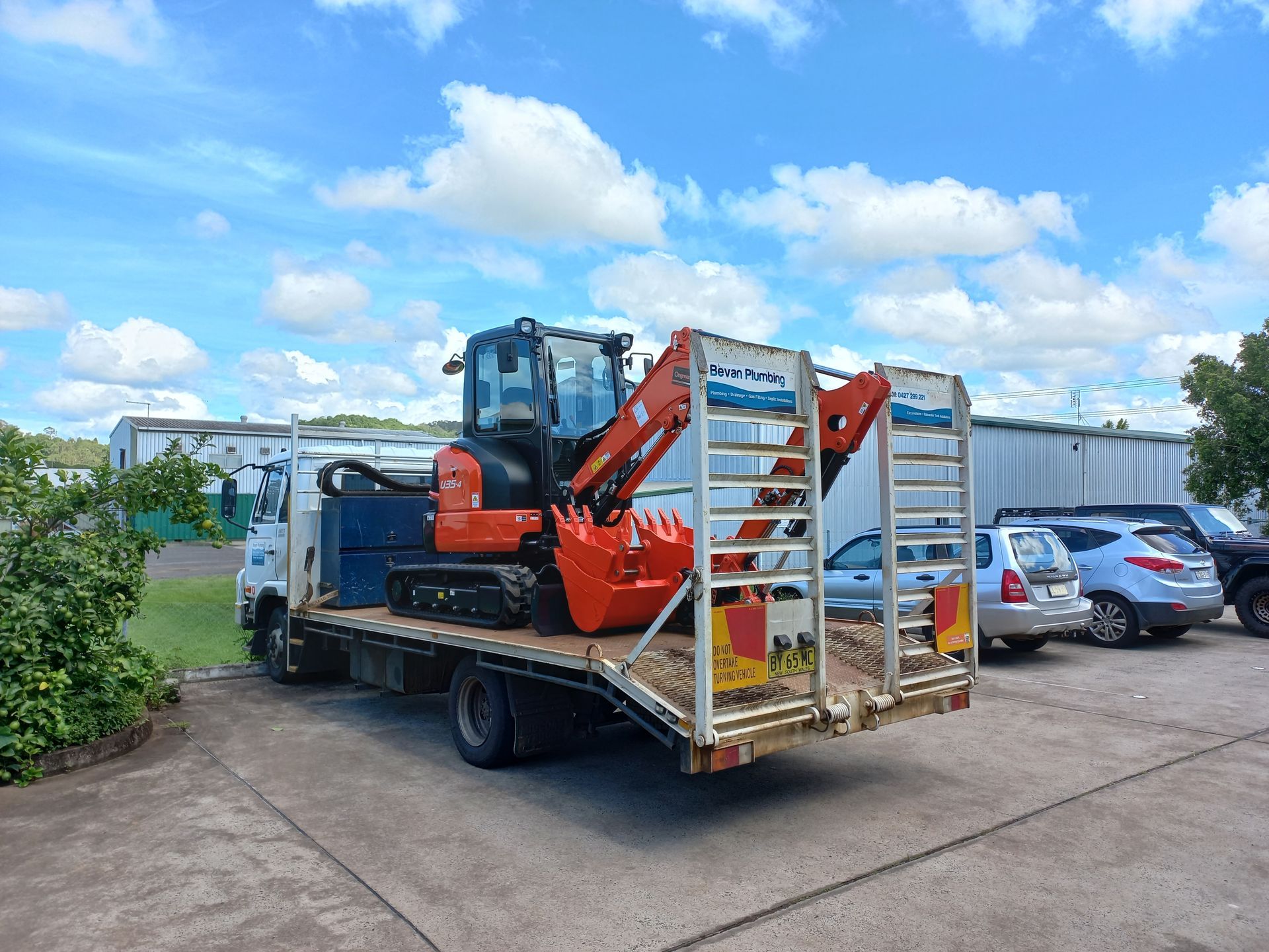 A Small Excavator is Sitting on the Back of a Flatbed Truck — Bevan Plumbing in South Lismore, NSW