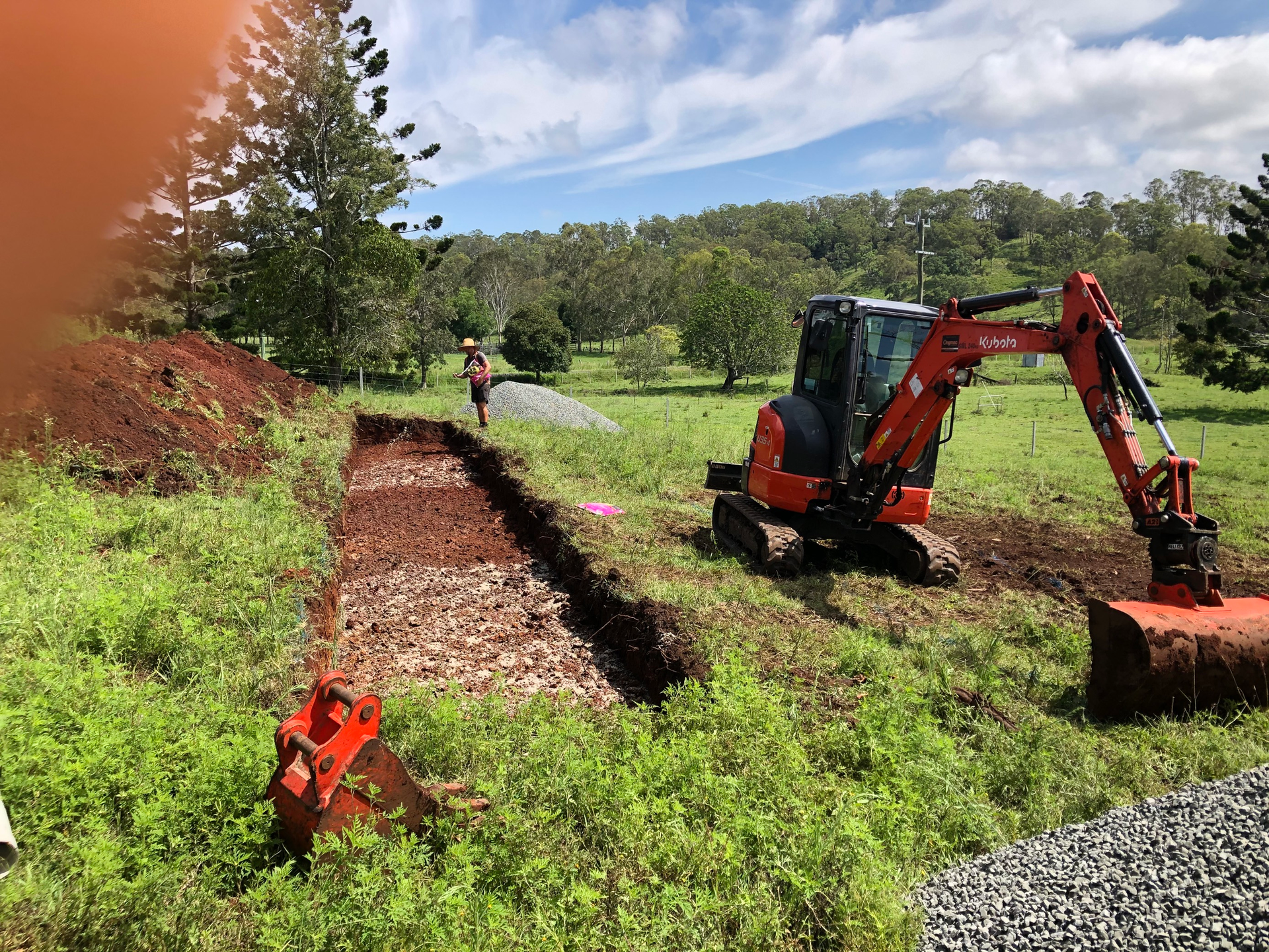 A Small Excavator is Digging a Hole in a Grassy Field — Bevan Plumbing in South Lismore, NSW