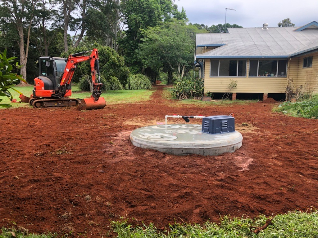 An Excavator is Digging a Hole in the Dirt in Front of a House — Bevan Plumbing in South Lismore, NSW