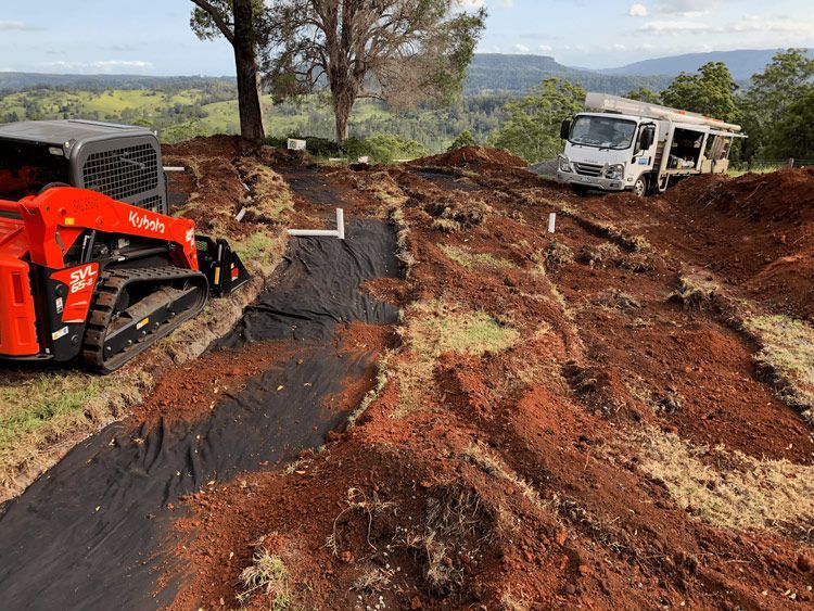 A Bulldozer is Driving Down a Dirt Road Next to a Truck — Bevan Plumbing in Alstonville, NSW
