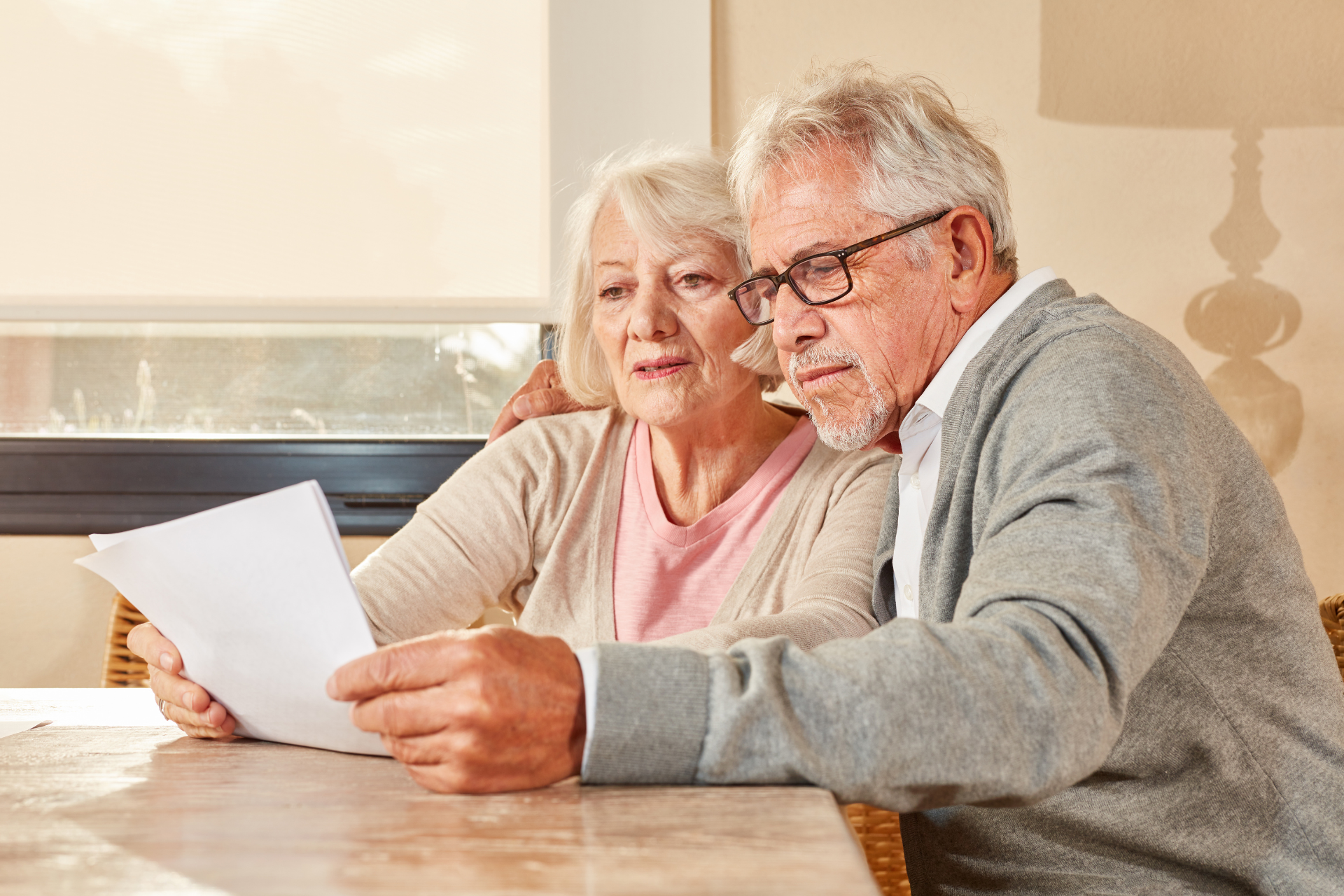 An elderly couple is sitting at a table looking at a piece of paper.