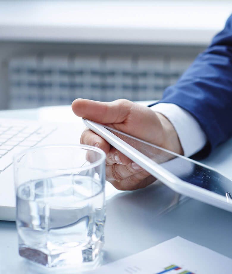 holding a tablet next to a laptop and glass of water on a desk