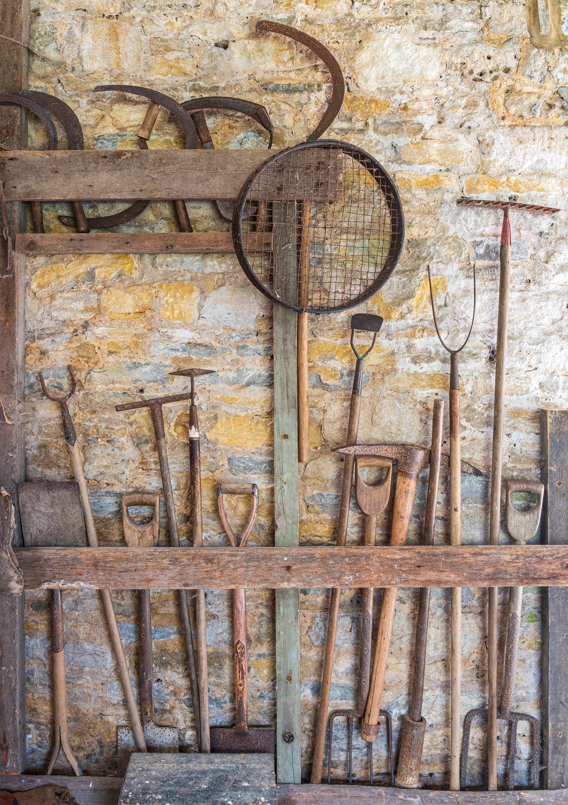 Rustic wall display of old farm tools and implements in a weathered wooden rack