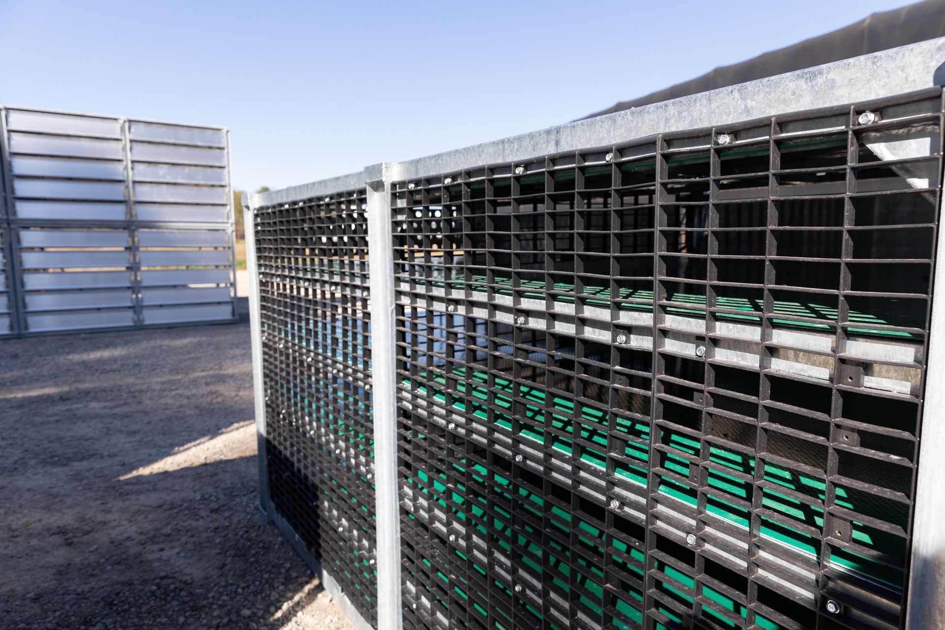 Caged containers with green objects inside, outdoors in a sunny setting. A second container is visible in the background.