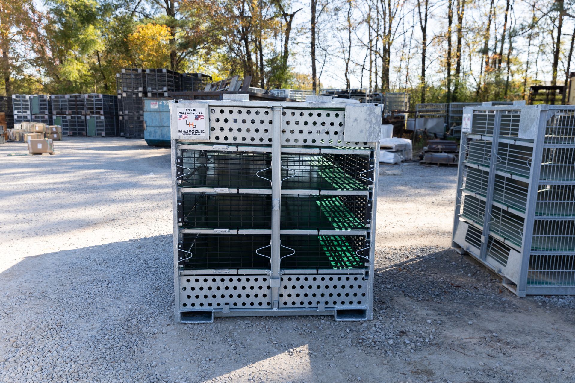 Close-up of a metal cage with a perforated base and a small opening, sitting on gravel.