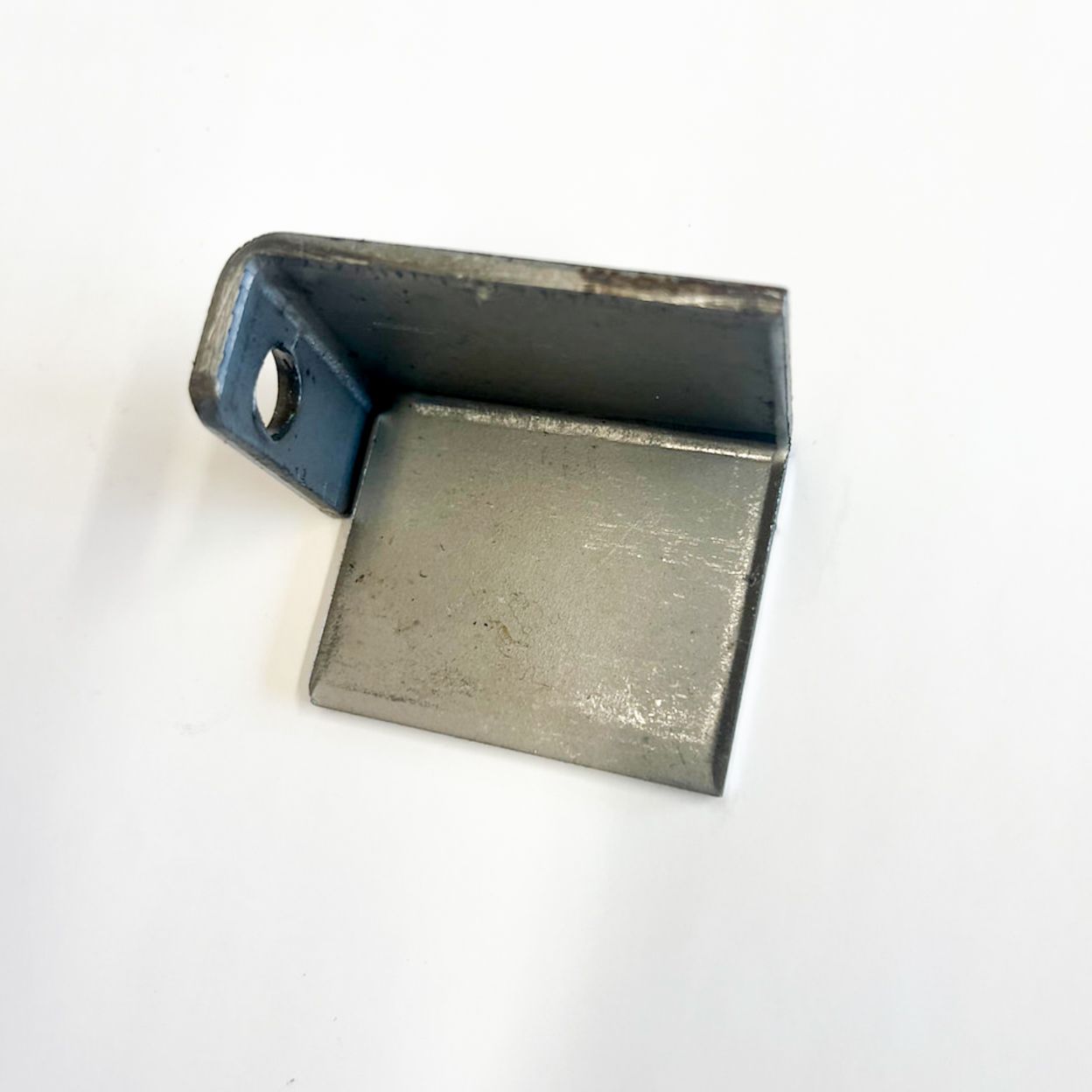 Metal L-shaped bracket with a hole, resting on a white surface.