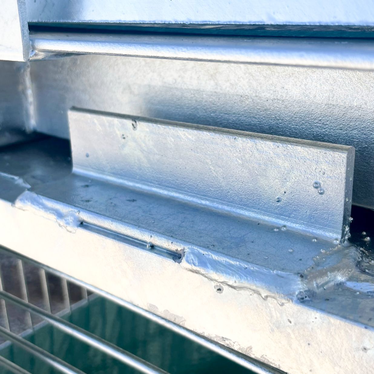 Galvanized metal bar welded to a metal frame, possibly a drain cover.
