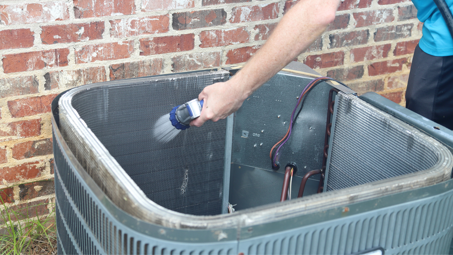A man is cleaning an air conditioner with a hose.