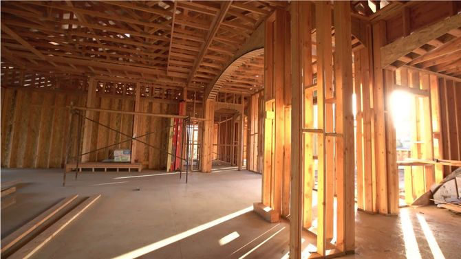 Unfinished wooden house interior framing with sunlit beams and open floor space