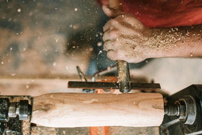 Hands shaping a wooden bowl on a lathe, with wood shavings flying in a workshop.