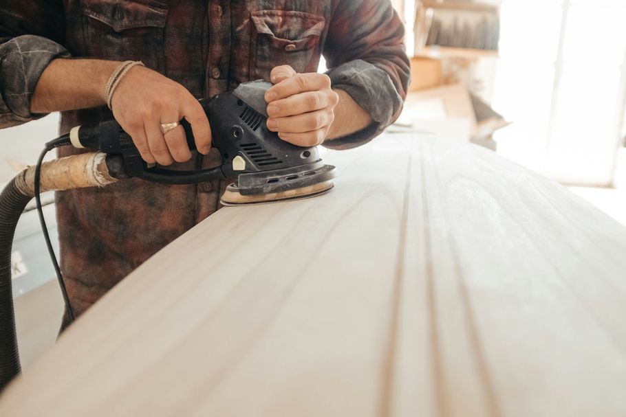 Person sanding a wooden plank with an orbital sander in a workshop
