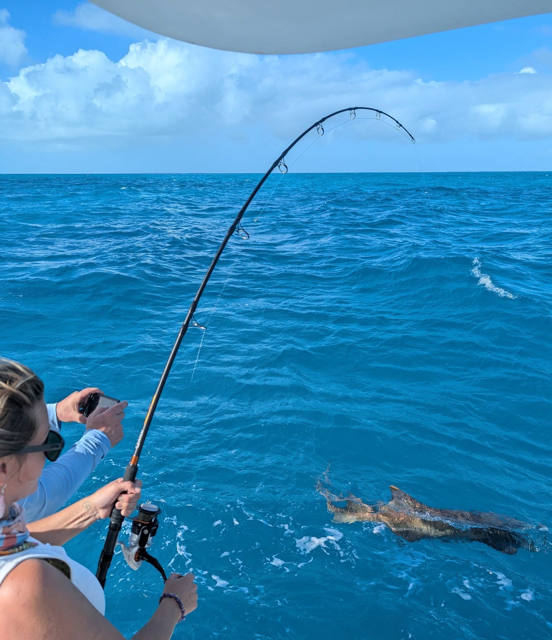 Person fishing on a boat beside a hooked fish in bright blue ocean water