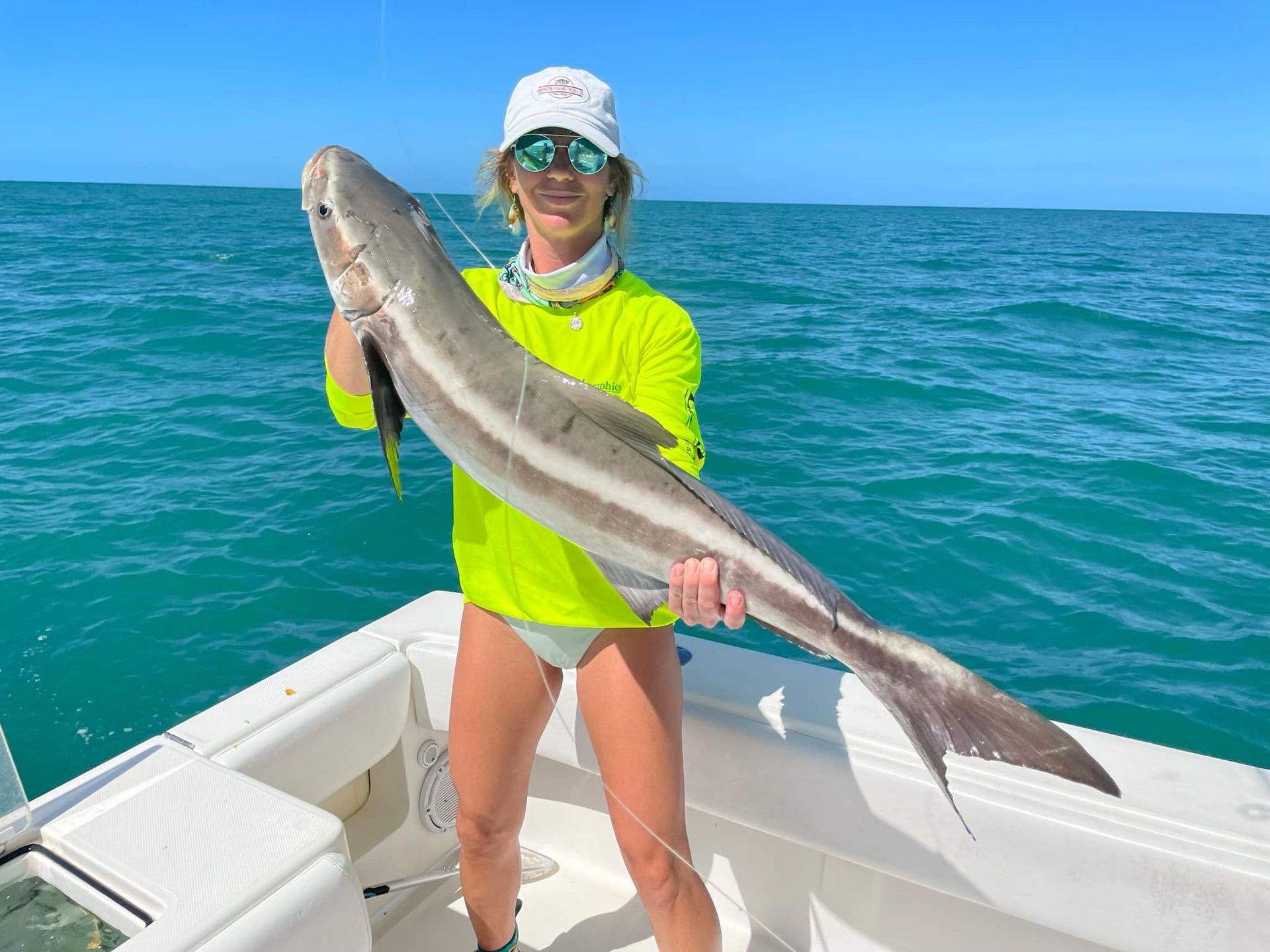 Person on a boat holding a large fish over blue ocean water