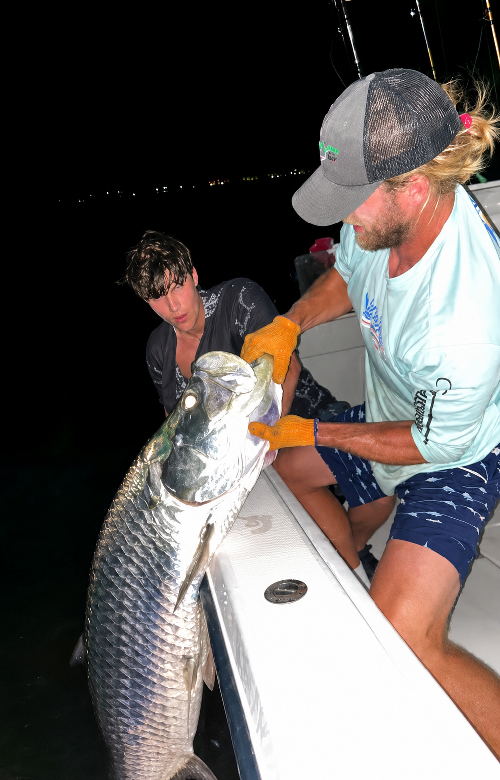 Two anglers on a boat holding a large fish at night