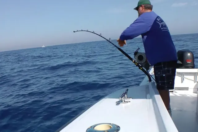 Angler in blue shirt reeling in a fish from a boat on open ocean