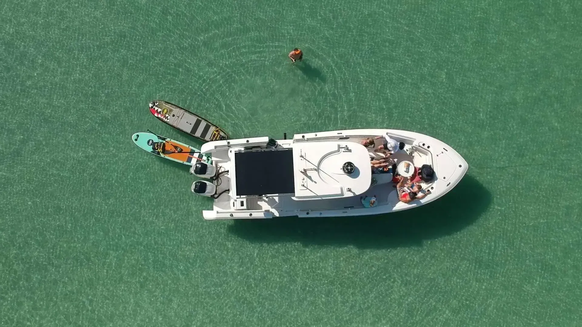 Overhead view of a small white boat on green water with a tiny person nearby