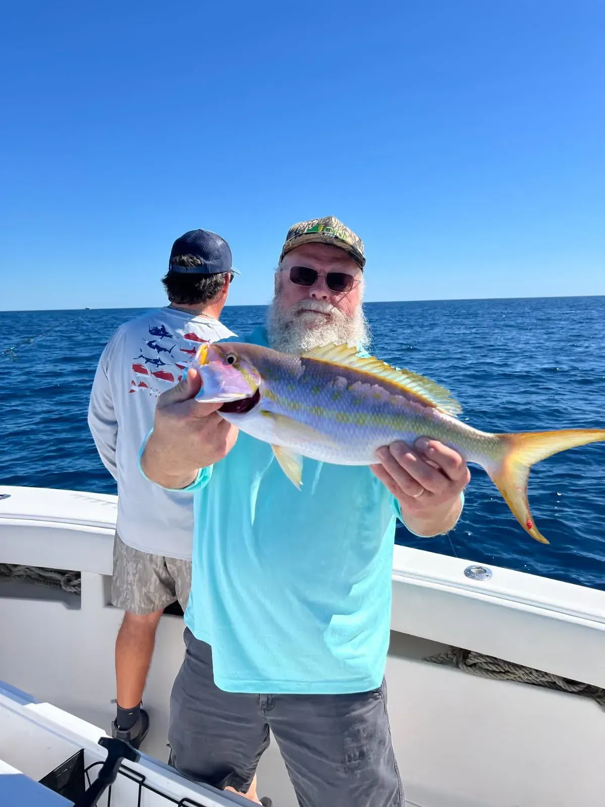 Man on a boat holds up a large fish with ocean and blue sky behind him