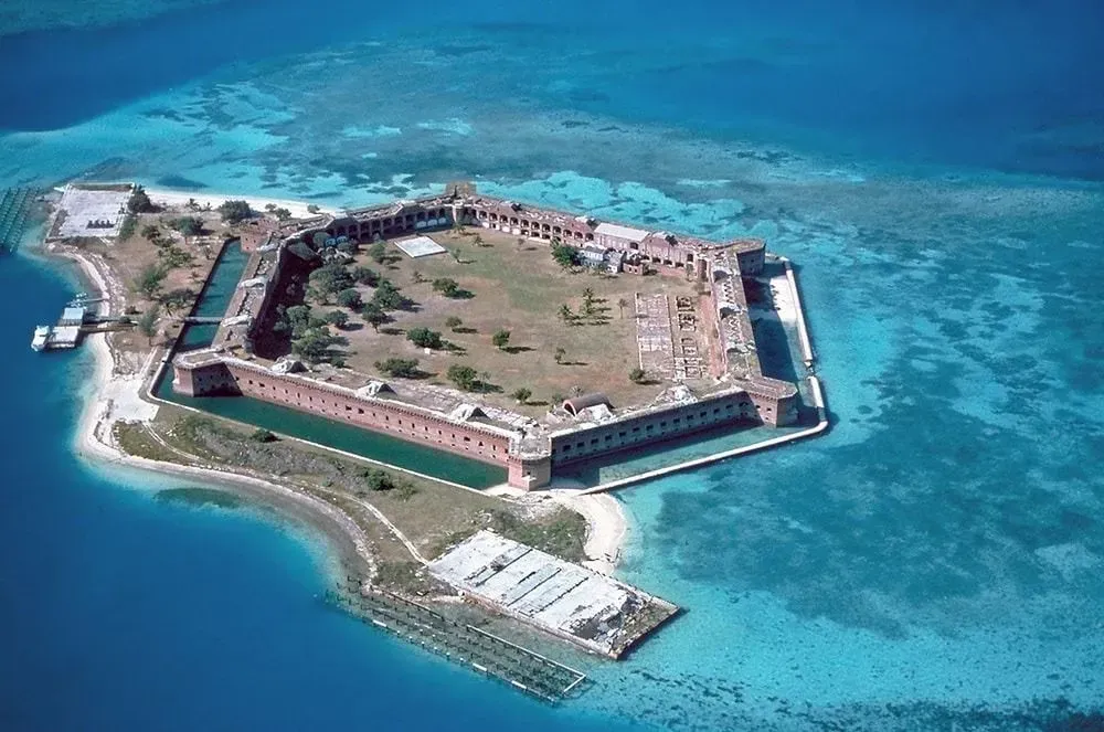 Aerial view of a small hexagonal island fort surrounded by bright turquoise water.