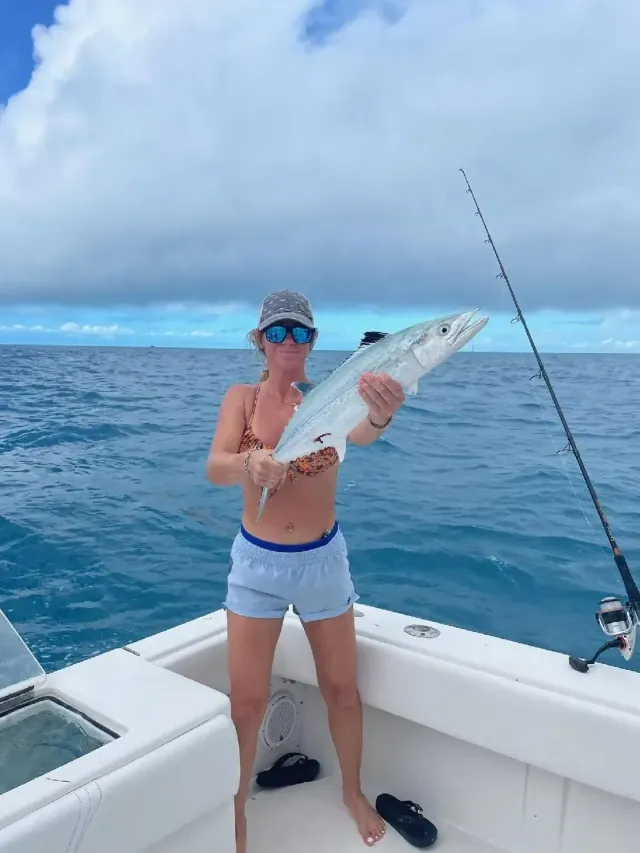 Person on a boat holding a large fish on the open ocean under a cloudy sky