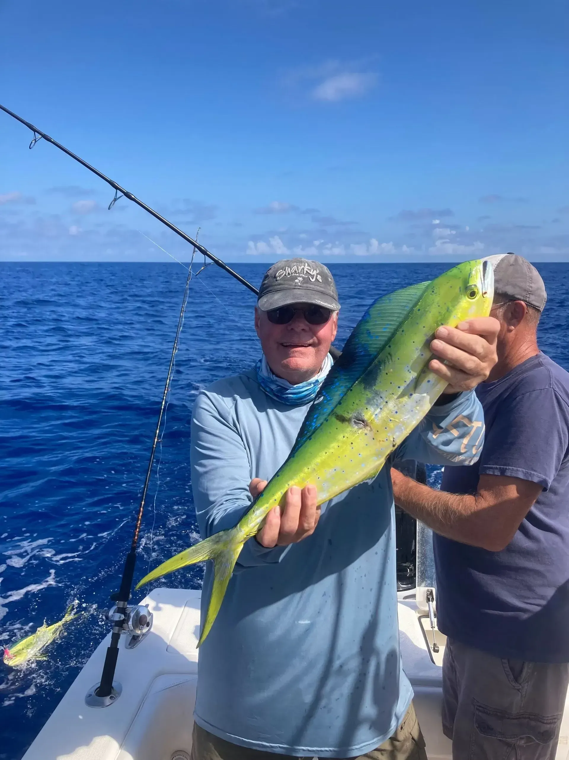 Two men on a boat holding a large green-yellow fish on a sunny ocean.