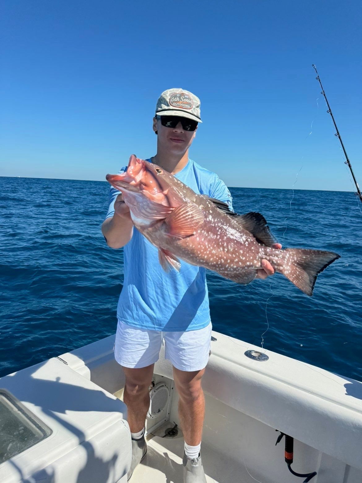 Person on a boat holding a large pink fish on a sunny blue ocean.