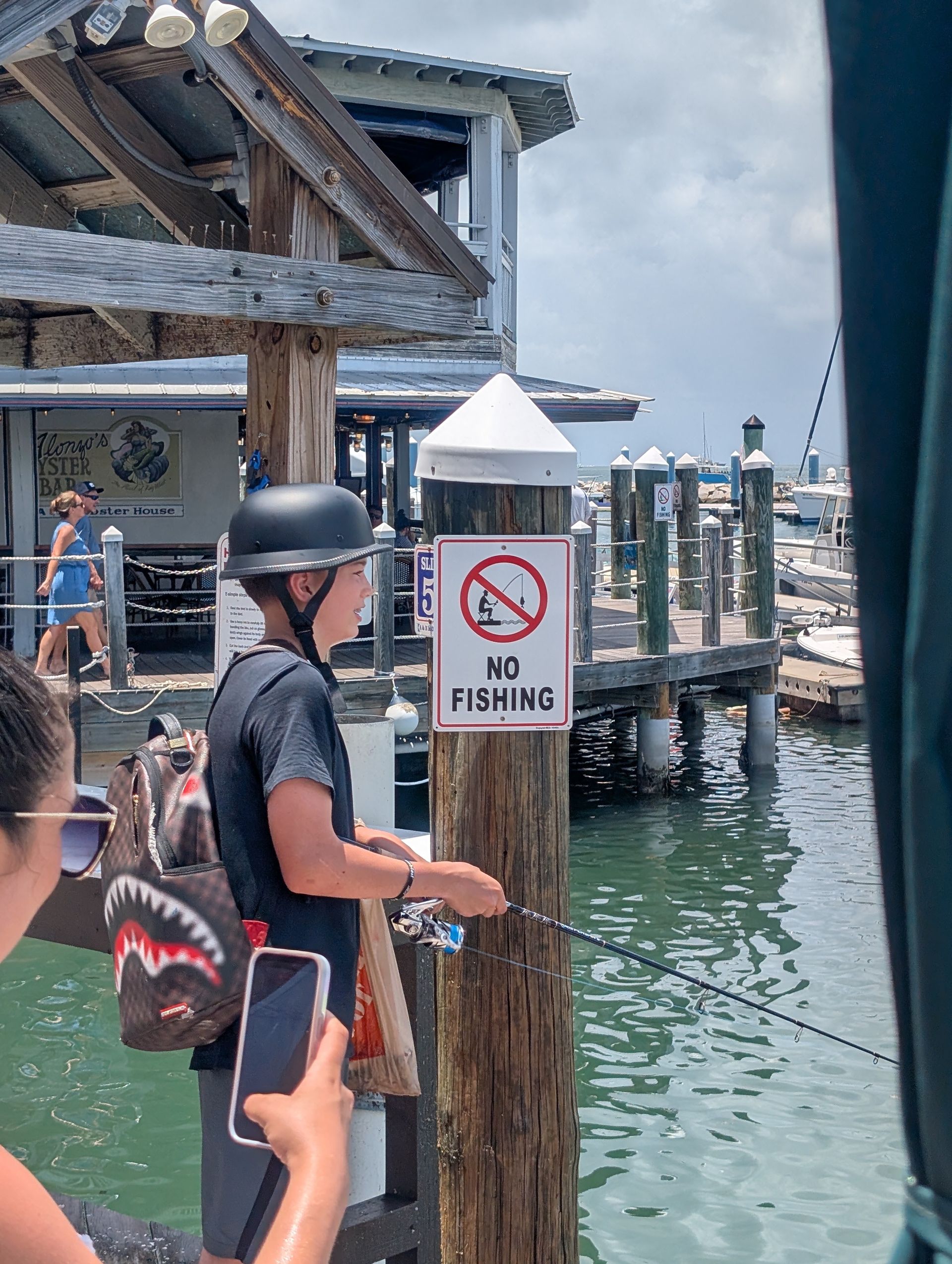 Person in a helmet near a “No Fishing” sign on a dock by the water.
