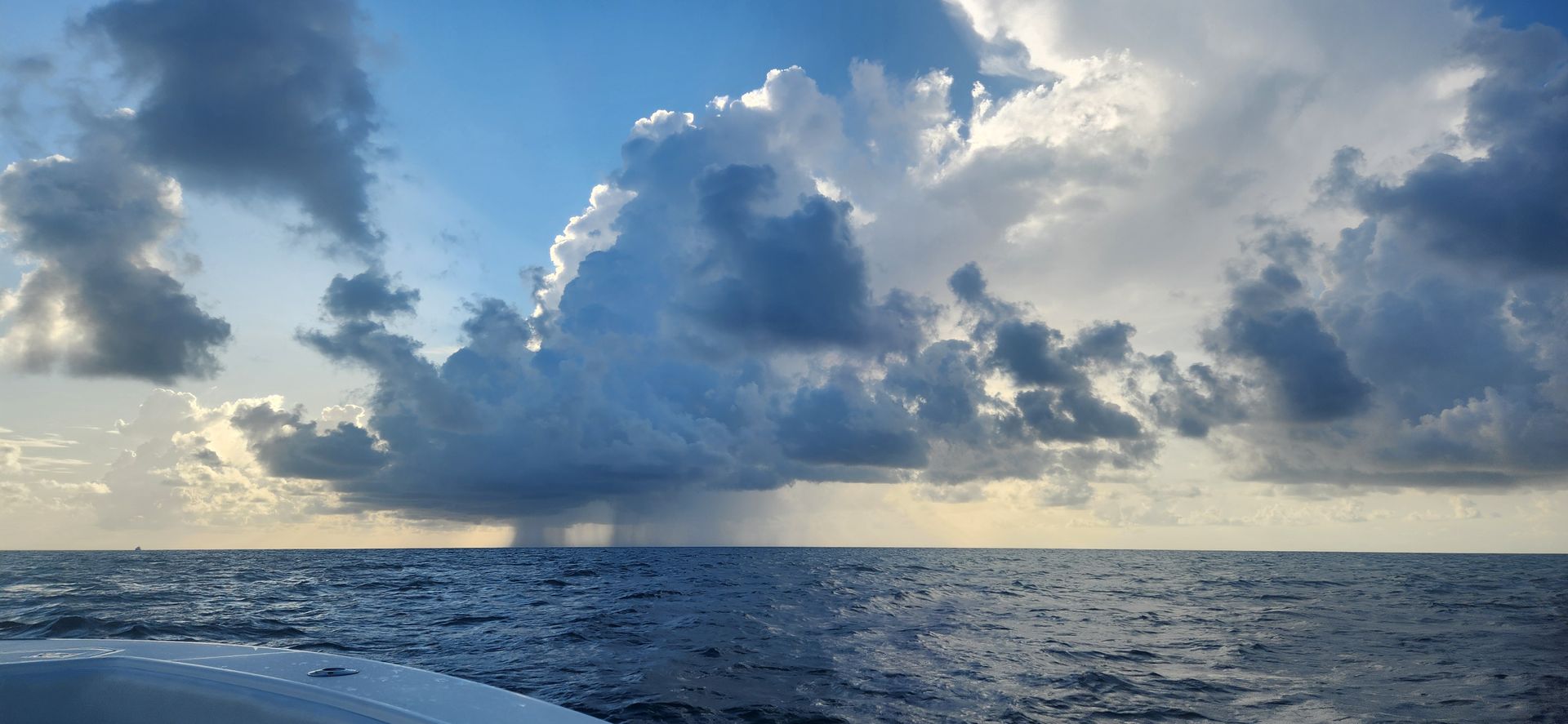 Rough ocean under dramatic cloudy sky, with the edge of a boat at left