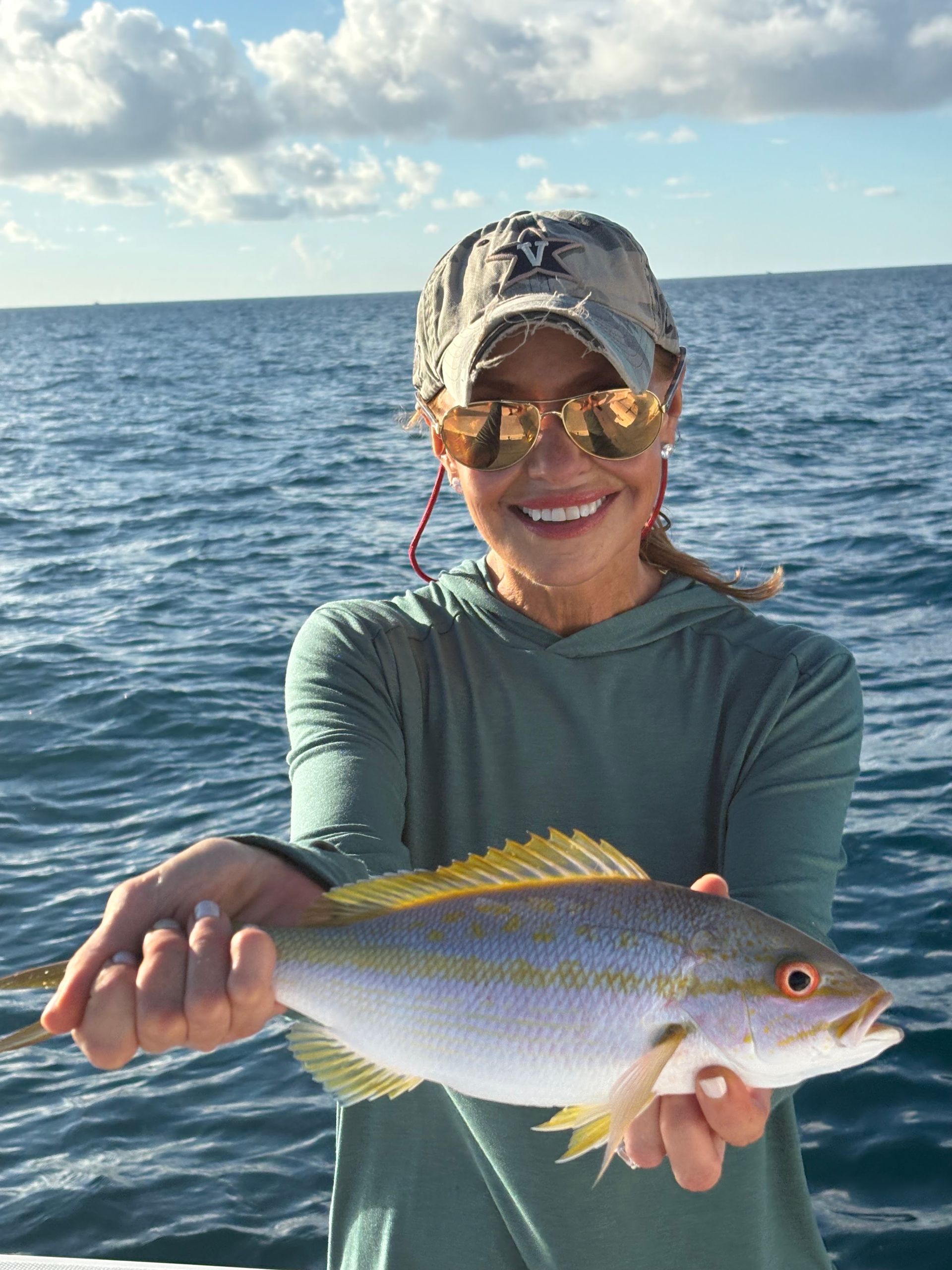 Smiling angler holding a silver fish on a boat with ocean and blue sky behind them
