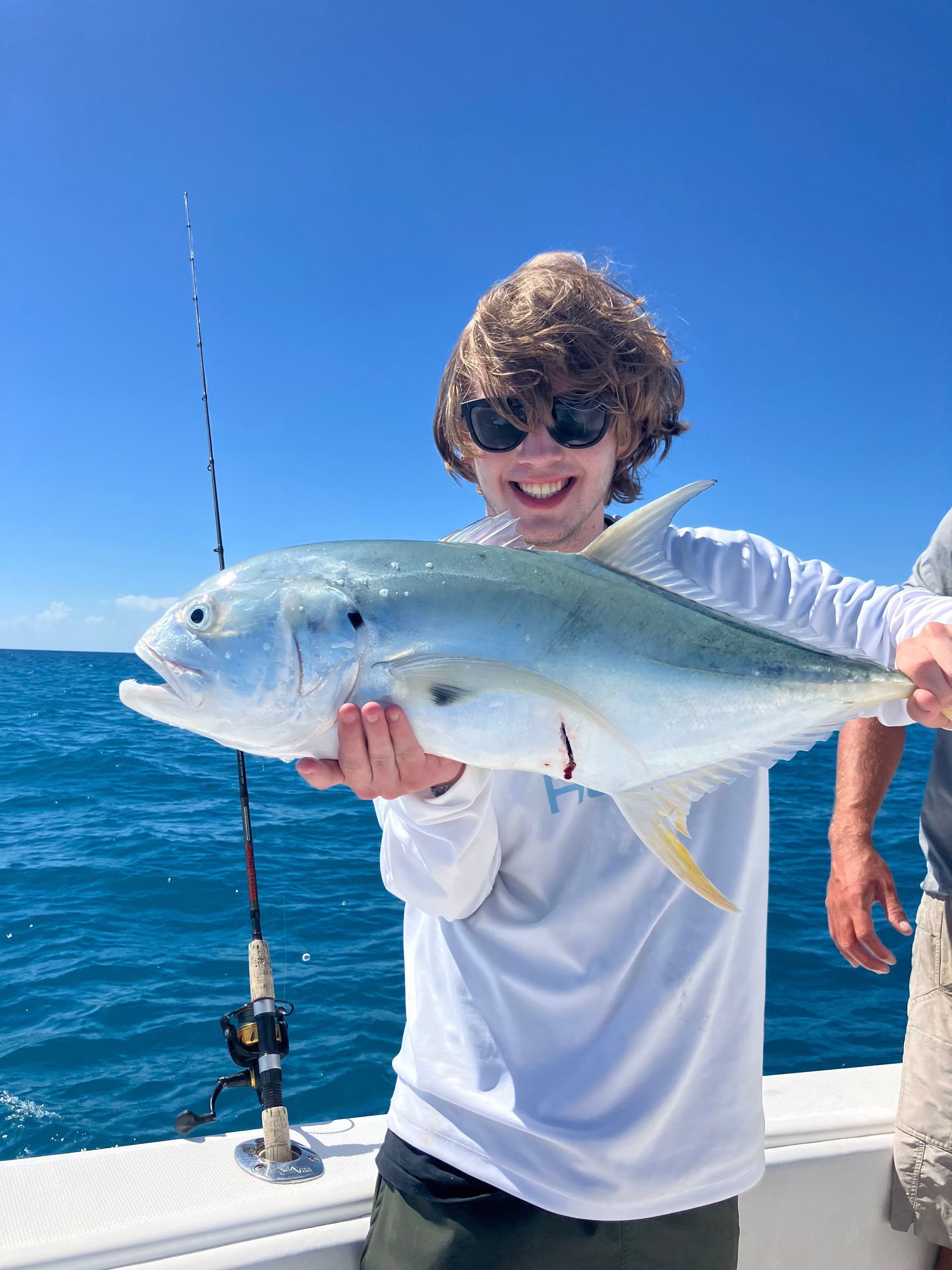 Person on a boat holding a large silver fish on a sunny blue ocean