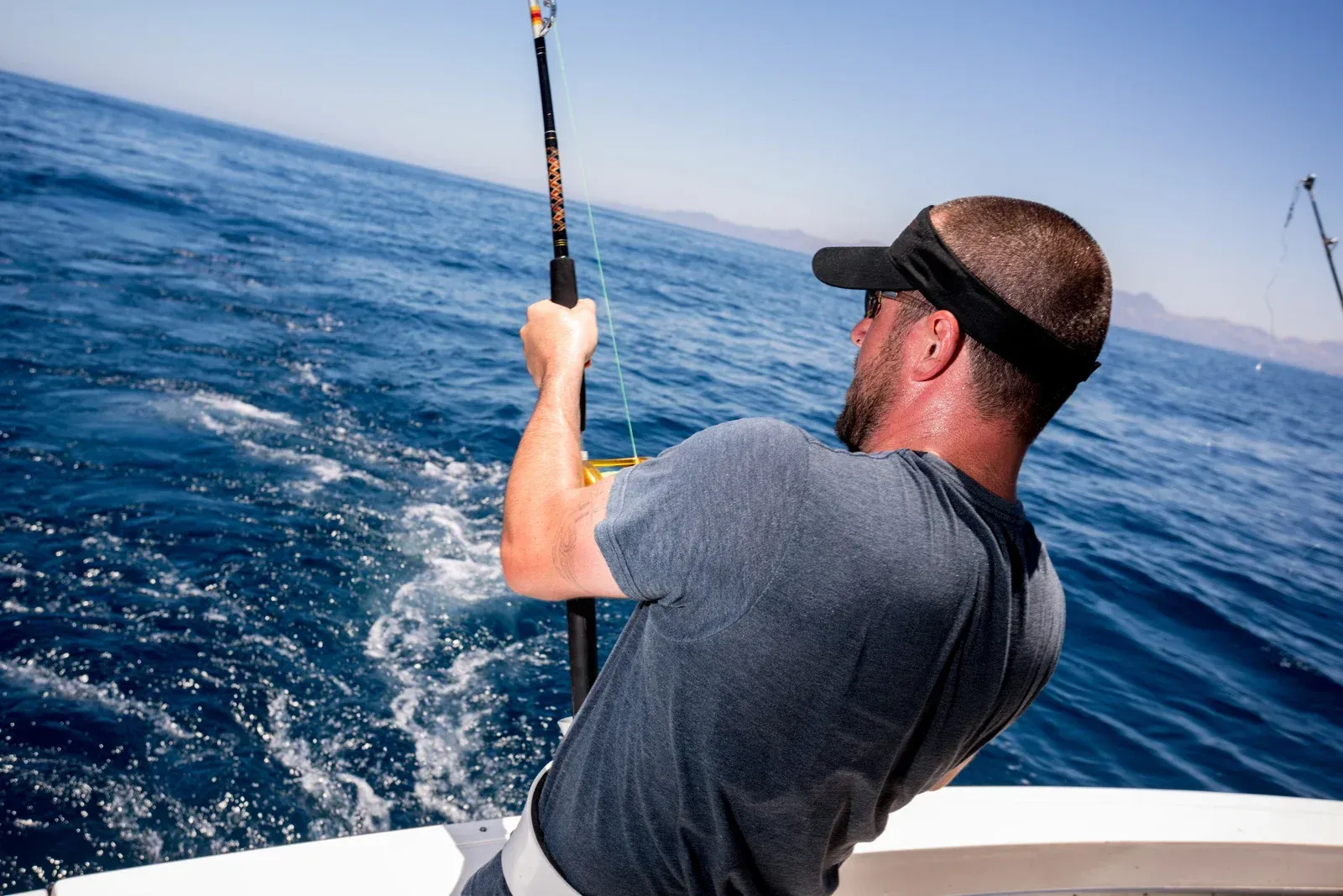 Person on a boat lifting a large fish from the blue ocean water