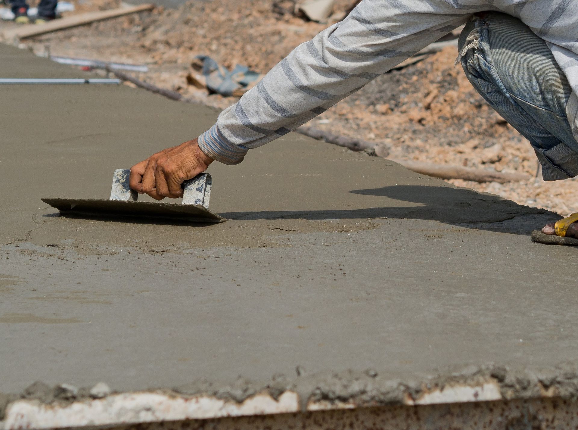 Worker smoothing wet concrete with a trowel at a construction site
