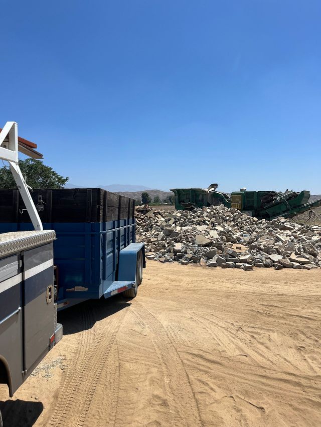 Yellow backhoe loader clearing rubble at a demolition site, kicking up dust.