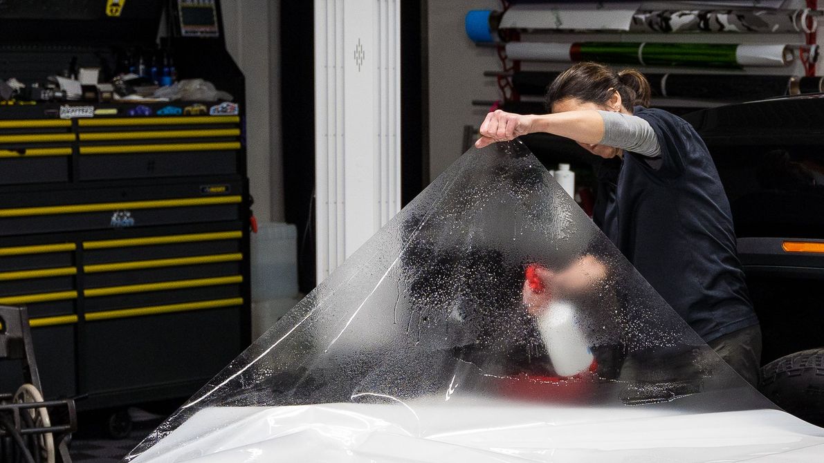 Wrapping a car with plastic wrap in a garage.