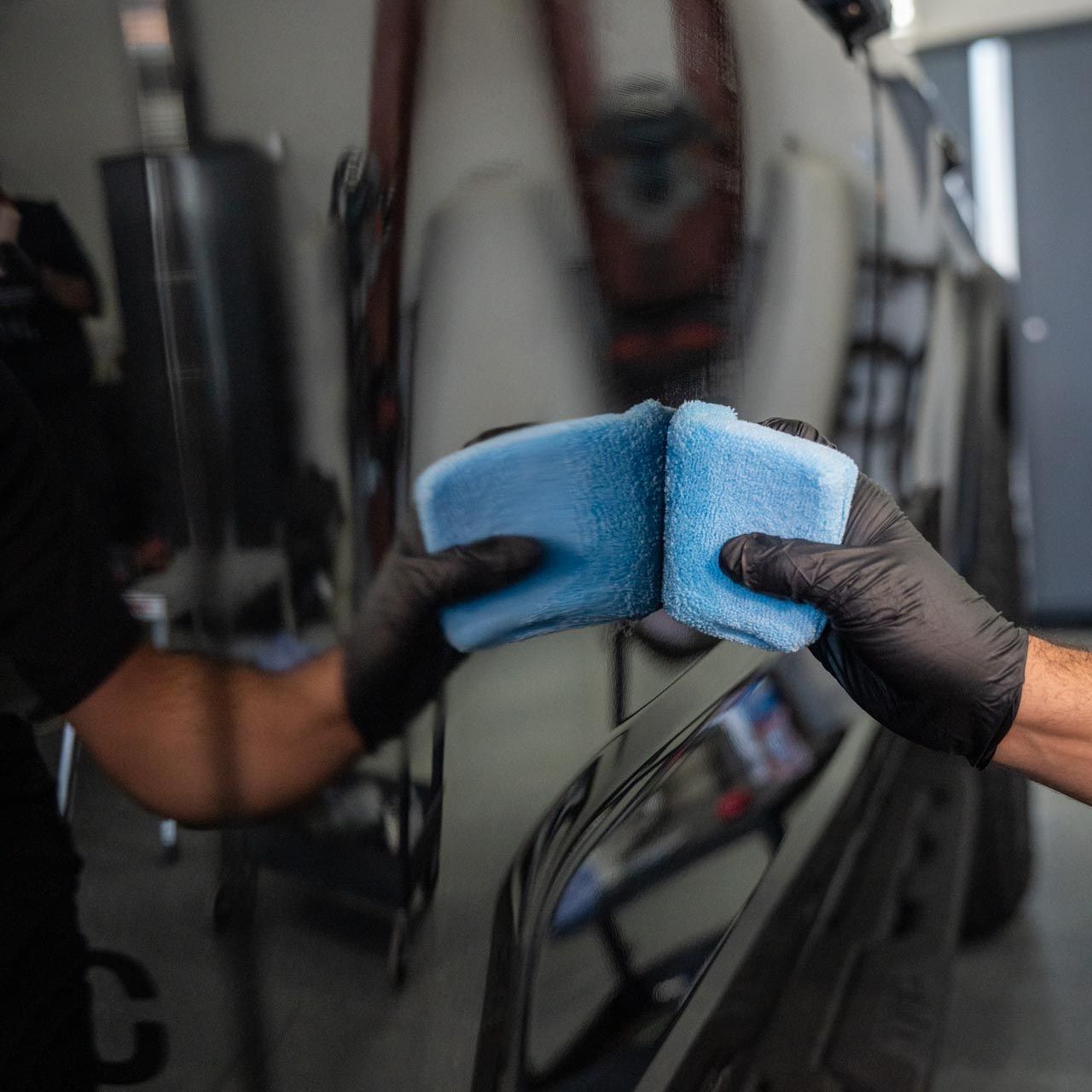 A person is holding a blue sponge in front of a car.