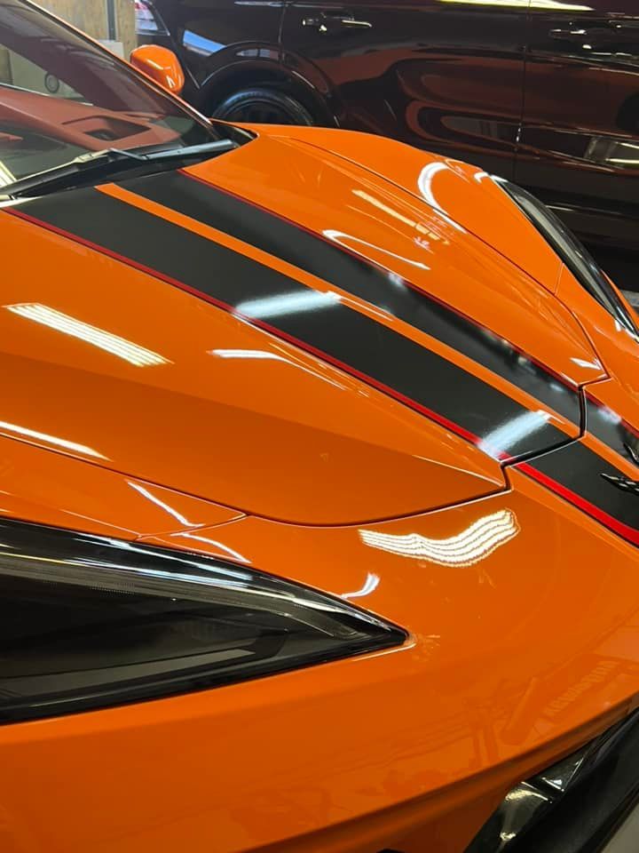 A close-up of an orange sports car with black stripes on the hood.