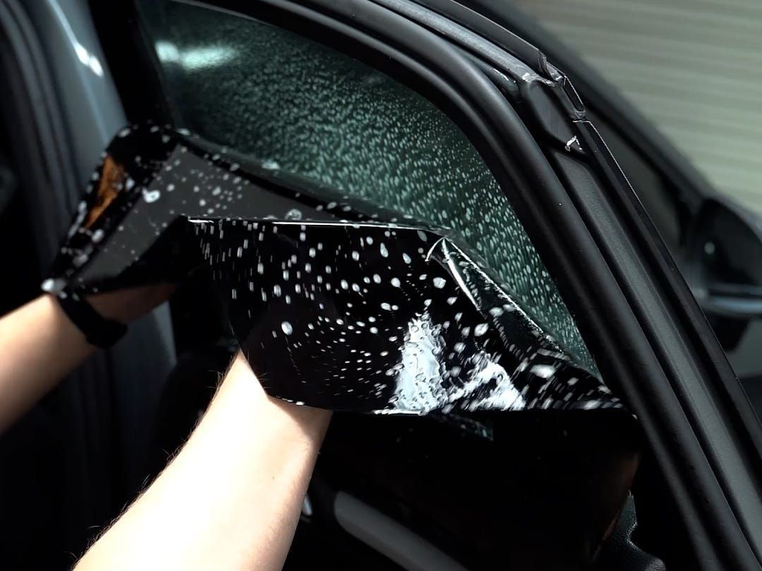 A  person is holding a piece of black plastic on a car window.