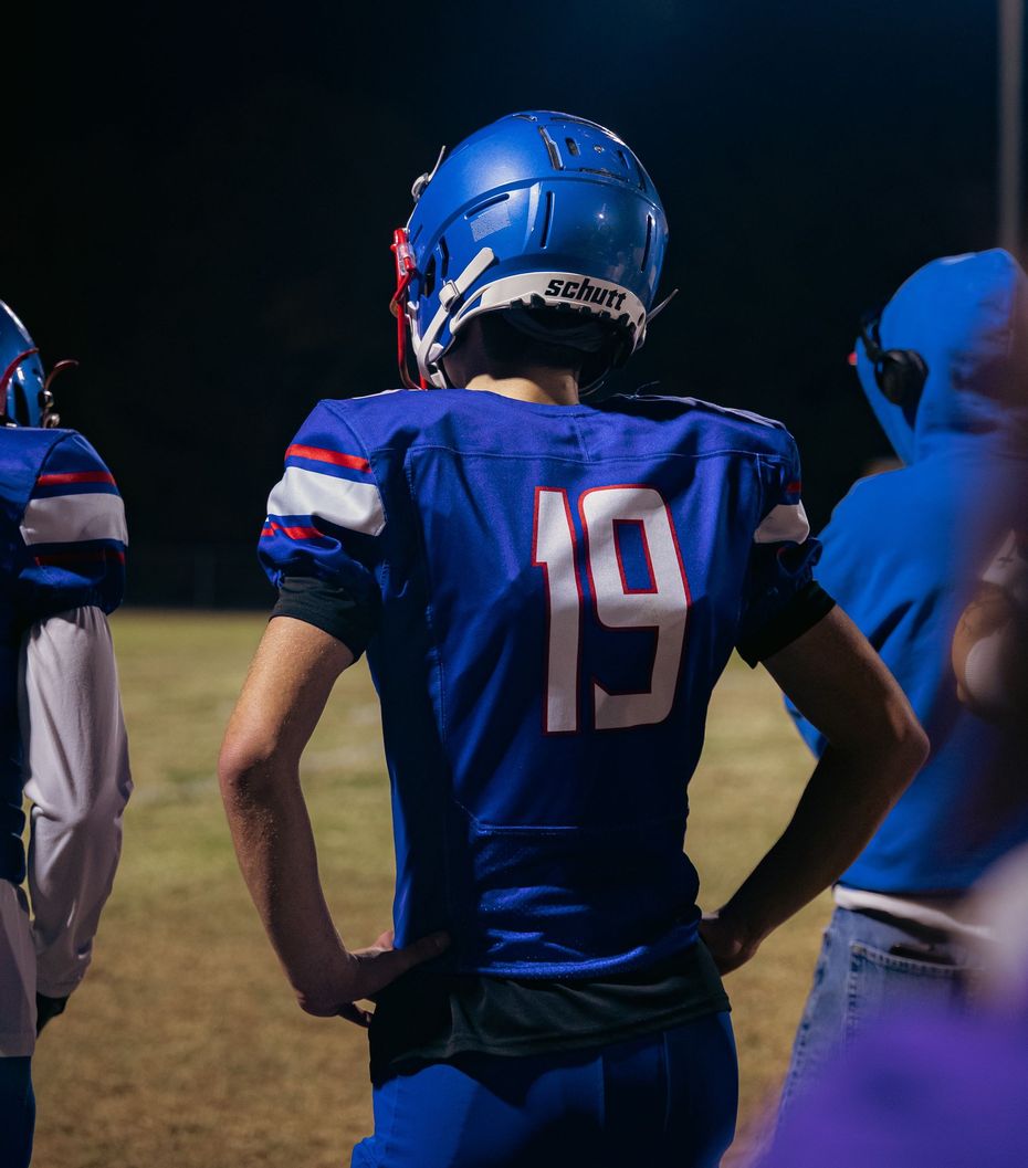 A football player wearing a blue jersey with the number 19 stands on a field at night.