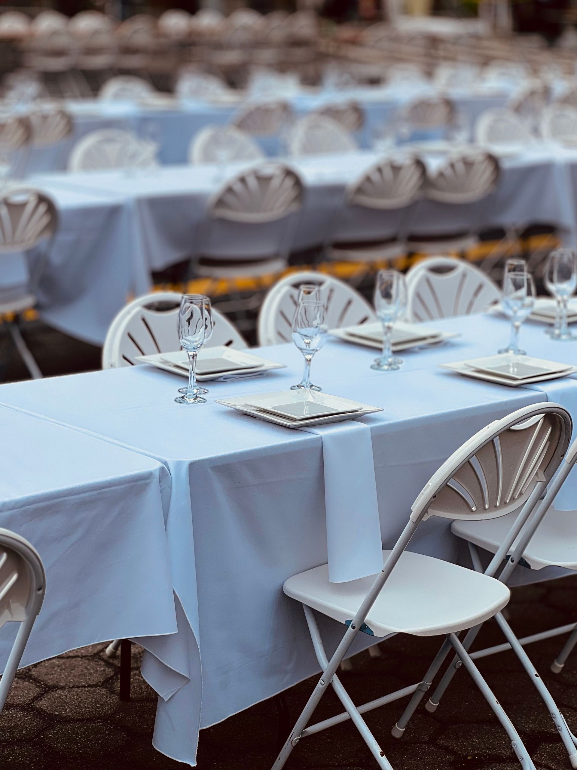 White-covered outdoor banquet tables with folded chairs set for an event